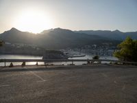 the sun is setting over a lake and mountain range near an asphalt road where the car is parked