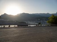 the sun is setting over a lake and mountain range near an asphalt road where the car is parked