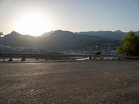 the sun is setting over a lake and mountain range near an asphalt road where the car is parked