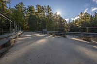 road with railing near the woods, bridge in the foreground and trees to the right of the photo