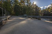 road with railing near the woods, bridge in the foreground and trees to the right of the photo