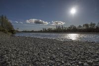 the sun shines over a river with large rocks in it on a sunny day