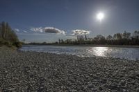 the sun shines over a river with large rocks in it on a sunny day