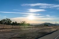 an empty road running towards the sun and mountains in the distance and a blue sky