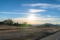 an empty road running towards the sun and mountains in the distance and a blue sky