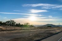 an empty road running towards the sun and mountains in the distance and a blue sky