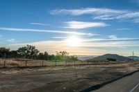 an empty road running towards the sun and mountains in the distance and a blue sky