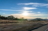 an empty road running towards the sun and mountains in the distance and a blue sky