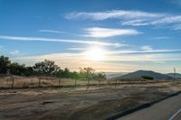 an empty road running towards the sun and mountains in the distance and a blue sky