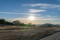 an empty road running towards the sun and mountains in the distance and a blue sky