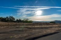 an empty road running towards the sun and mountains in the distance and a blue sky