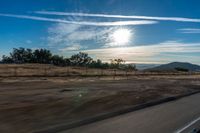 an empty road running towards the sun and mountains in the distance and a blue sky