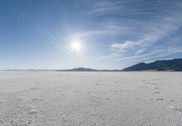 the snow has footprints in it and the sun is shining on the horizon to the mountains