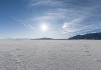 the snow has footprints in it and the sun is shining on the horizon to the mountains