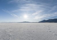 the snow has footprints in it and the sun is shining on the horizon to the mountains