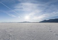 the snow has footprints in it and the sun is shining on the horizon to the mountains