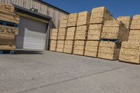 a pile of bundles of stacked logs in front of a warehouse door near a truck