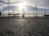 the sun shines on a cobblestone road with a bench and benches in front