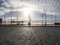 the sun shines on a cobblestone road with a bench and benches in front