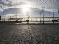 the sun shines on a cobblestone road with a bench and benches in front