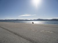 a person sitting on the beach in front of the ocean, looking at the water