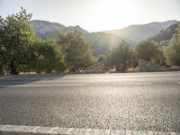 the sun shines on an empty road near a gate and tree covered mountain range