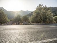 the sun shines on an empty road near a gate and tree covered mountain range