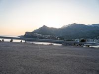 a bicycle parked near the side of a road at sunset by the water and mountain range