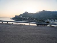 a bicycle parked near the side of a road at sunset by the water and mountain range