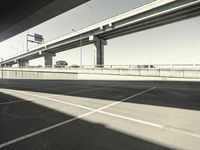 an empty parking lot and bridge from beneath it looking at the city below it with traffic lights