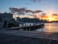 a person is sitting on a bench at the dock with a sunset in the background