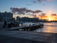 a person is sitting on a bench at the dock with a sunset in the background