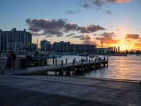 a person is sitting on a bench at the dock with a sunset in the background