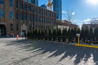 a sidewalk in front of an industrial building with trees near it, with a construction crane behind a gate and another building