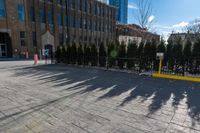 a sidewalk in front of an industrial building with trees near it, with a construction crane behind a gate and another building