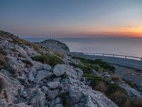 a curved road going along the sea as the sun set on the horizon behind it