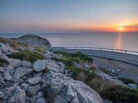 a curved road going along the sea as the sun set on the horizon behind it