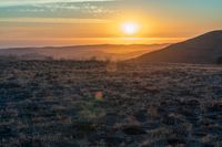 there is a sunset in the horizon on a field with grassy land below the mountains