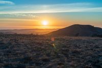 there is a sunset in the horizon on a field with grassy land below the mountains