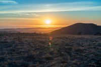 there is a sunset in the horizon on a field with grassy land below the mountains