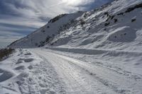 a person on skis on a snowy road with mountains in the background, and lots of snow all around