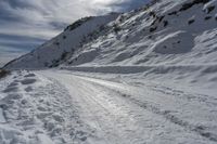 a person on skis on a snowy road with mountains in the background, and lots of snow all around