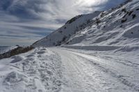 a person on skis on a snowy road with mountains in the background, and lots of snow all around