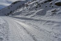 a person on skis on a snowy road with mountains in the background, and lots of snow all around