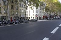 a bunch of scooters line the streets of paris on a sunny day and one person rides a bicycle with no helmet