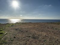 a large sandy field by the water on a sunny day, with sun shining over the ocean