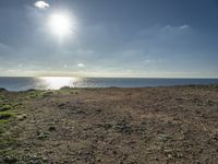 a large sandy field by the water on a sunny day, with sun shining over the ocean