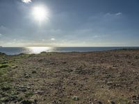 a large sandy field by the water on a sunny day, with sun shining over the ocean