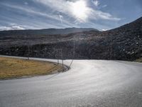 a curved asphalt road with hills in the background on an overcast day with sun shining