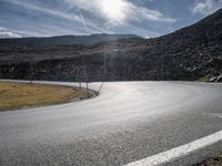 a curved asphalt road with hills in the background on an overcast day with sun shining